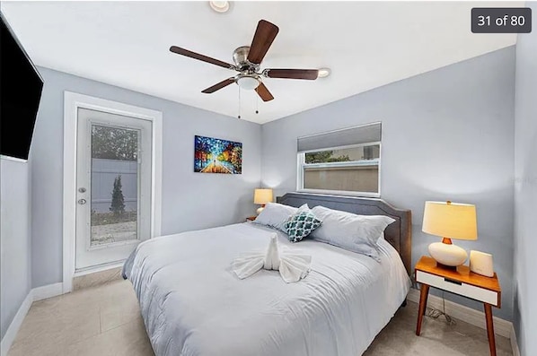 A bedroom with a bed, a ceiling fan, a nightstand with a lamp, and a window. - 1st floor apt B. 1 mile from waterfront and downtown. Just 2 miles from beach! (Sarasota)