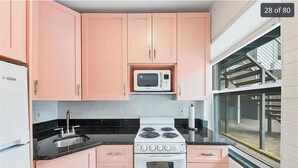 A kitchen with pink cabinets, a white stove, a microwave, and a window with a view of a building.