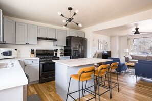 Une cuisine moderne avec des meubles gris, un îlot central doté de tabourets de bar, un four encastré et un réfrigérateur noir.