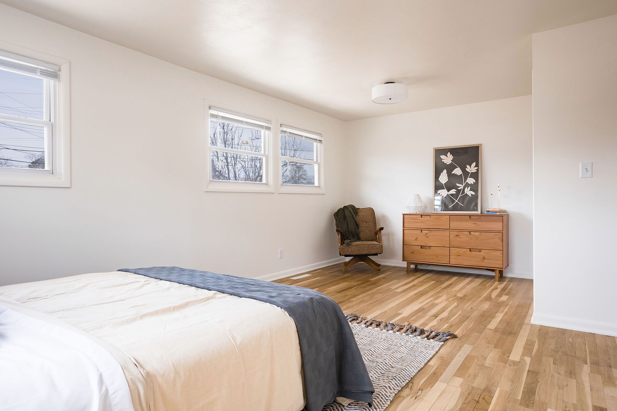 A bedroom with a bed, dresser, chair, and two windows.