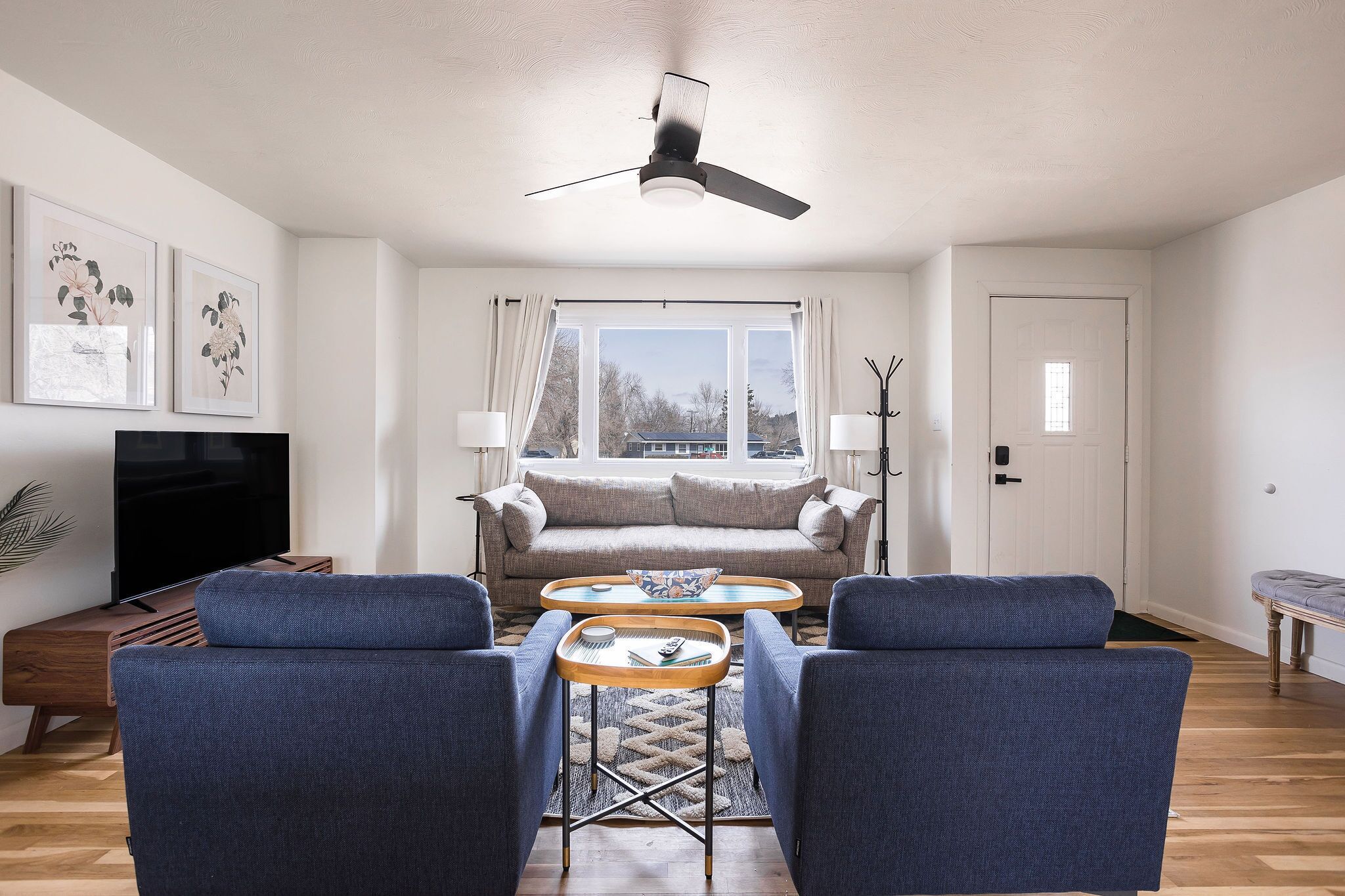 A living room with a sofa, two armchairs, a coffee table, a TV, and a ceiling fan.