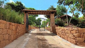 A stone pathway leading to a gated entrance with a tiled roof structure. - Color Marrón (Barichara)