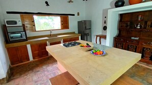 A kitchen with a central island, a microwave, a toaster, a refrigerator, and a window with a view of trees. - Color Marrón (Barichara)