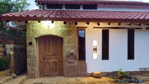 A stone building with a wooden door and a red-tiled roof. - Color Marrón (Barichara)