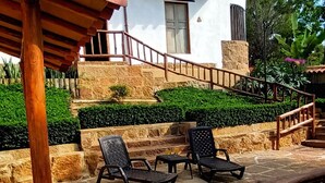 A house with a stone patio, outdoor seating, and a wooden pergola. - Color Marrón (Barichara)