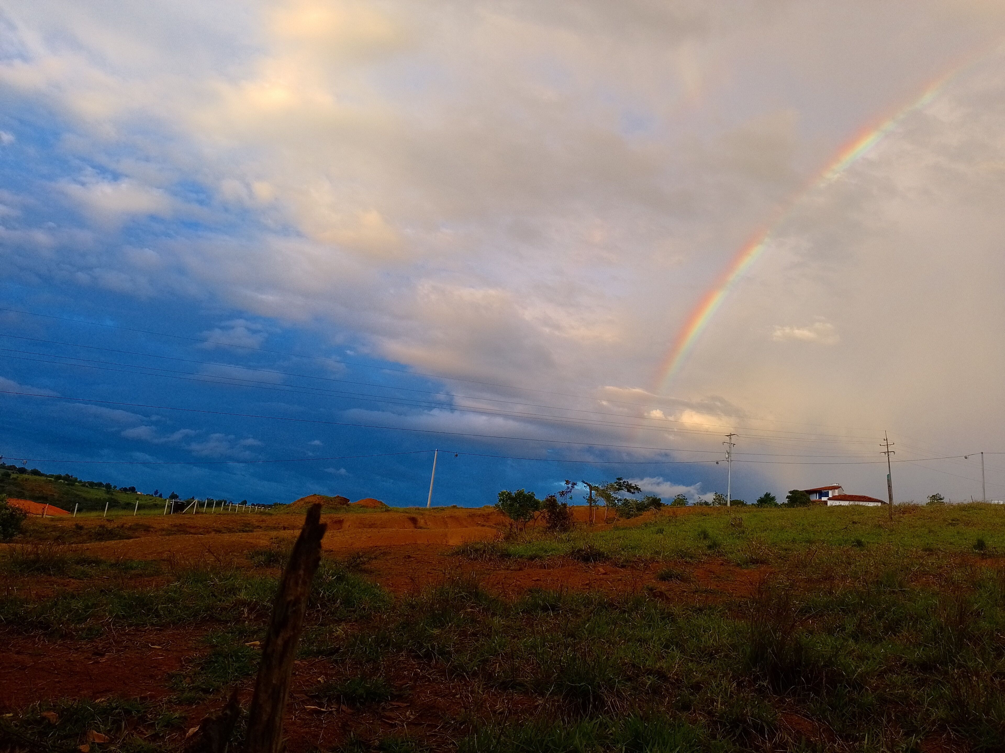 A rural landscape with a rainbow, power lines, and a dirt road.