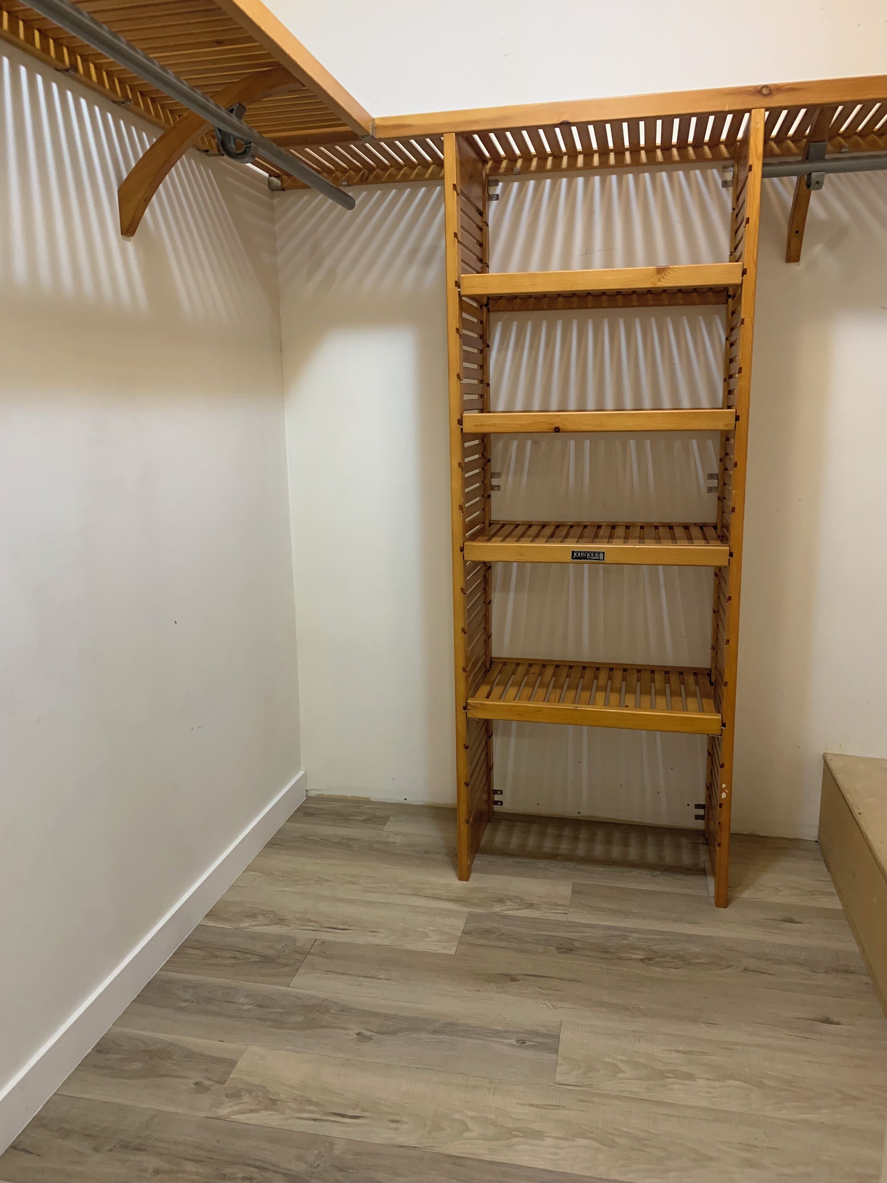 A wooden shelving unit with three shelves in a corner of a room with wooden flooring and white walls.