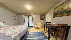 A bedroom with a bed, a desk, a chair, a dining table, and a painting on the wall.