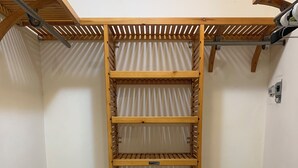 A wooden shelving unit with three shelves and a bench, in a room with wooden flooring and white walls.