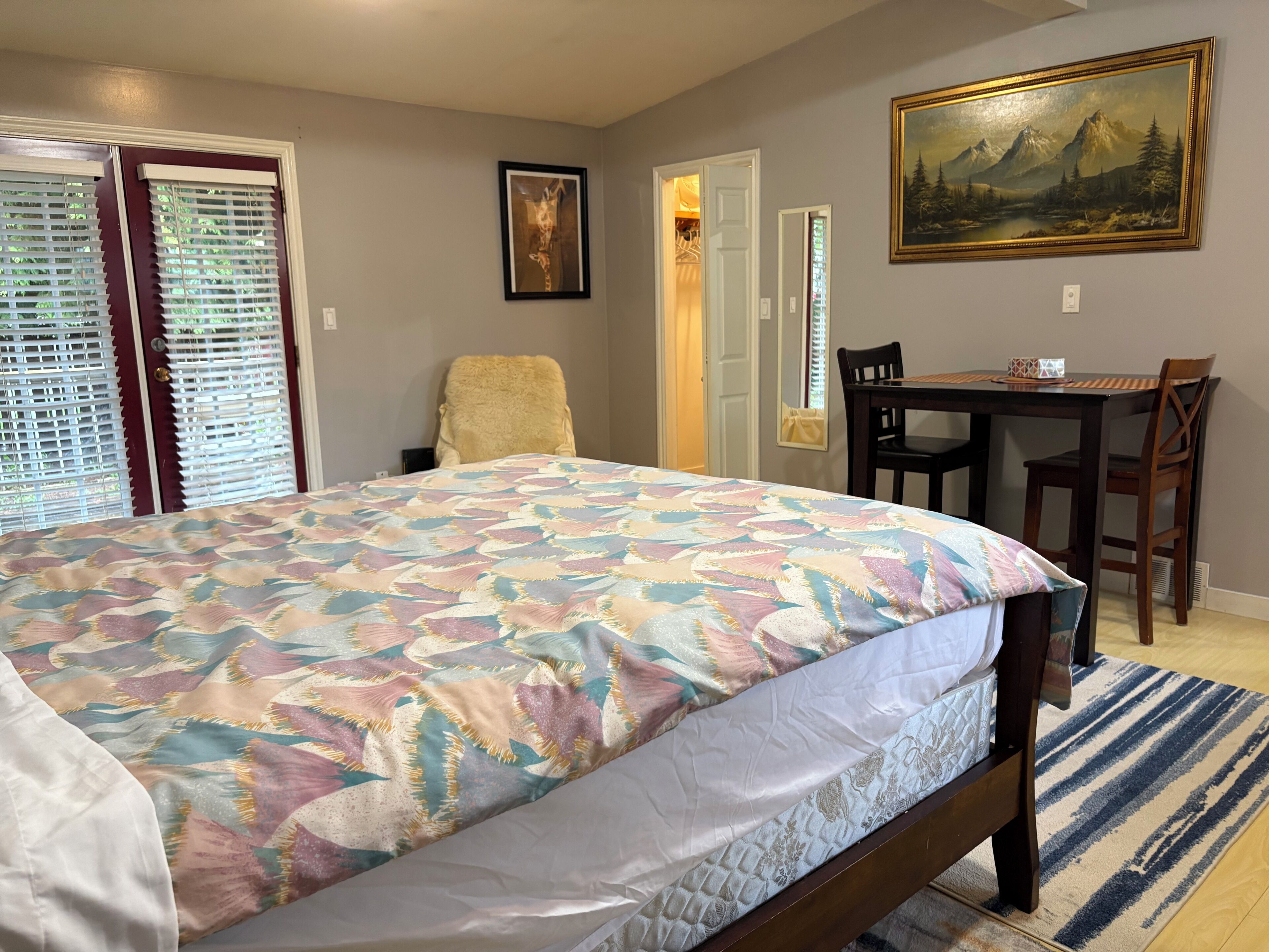 Un dormitorio con cama, una silla, una mesa y un cuadro en la pared.