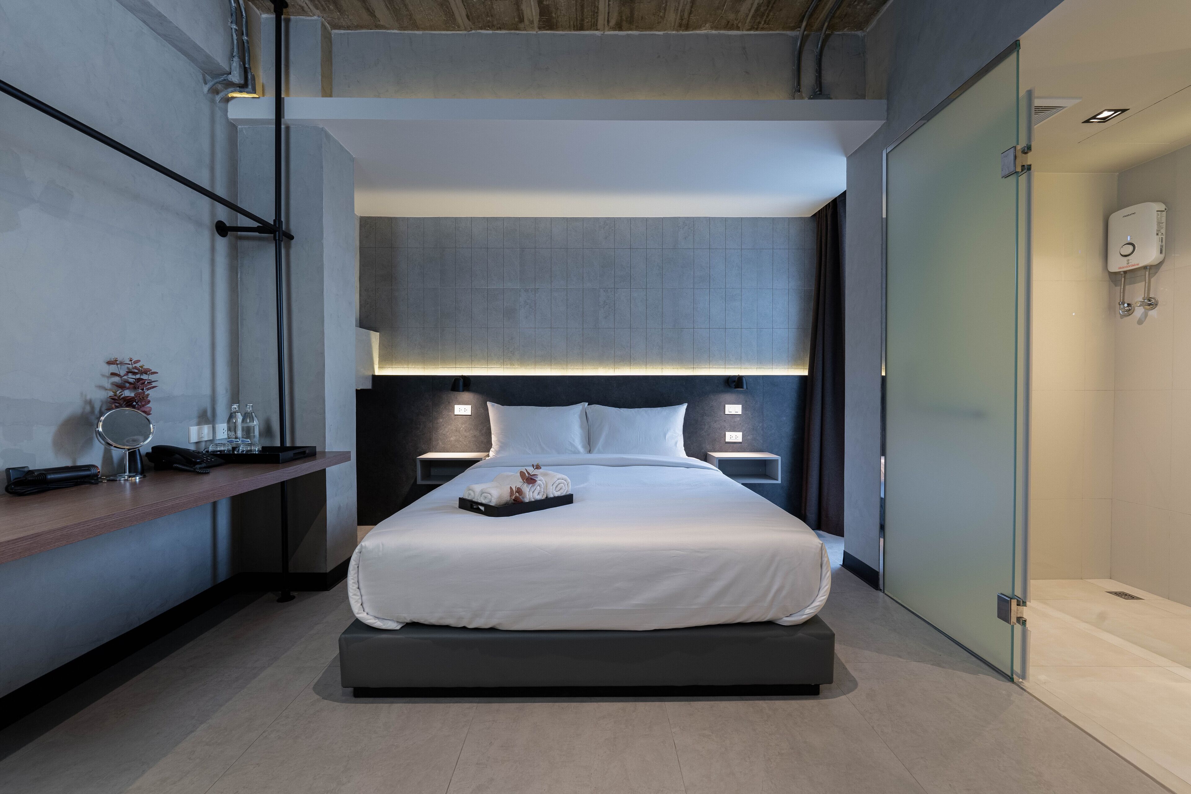 A modern hotel room with a large bed, bedside tables, a small desk, and a glass partition wall.