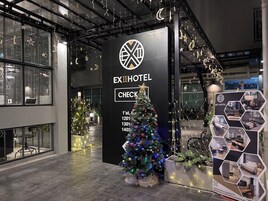 Exterior del EXIHOTEL con un árbol de Navidad, un mostrador de recepción y una exhibición de interiores de habitaciones.