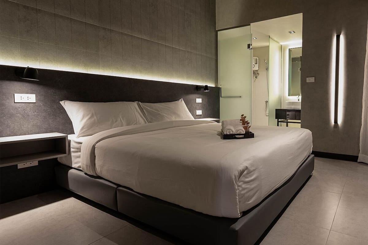 Quarto de hotel moderno com uma cama grande, mesas de cabeceira, um espelho e área de chuveiro.