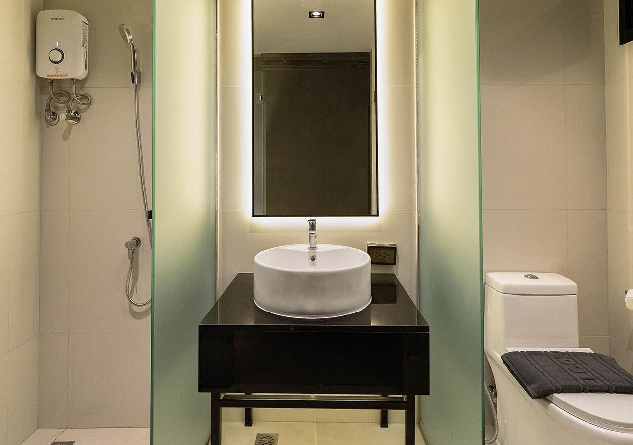 A modern bathroom with a round sink, a handheld showerhead, and a toilet.