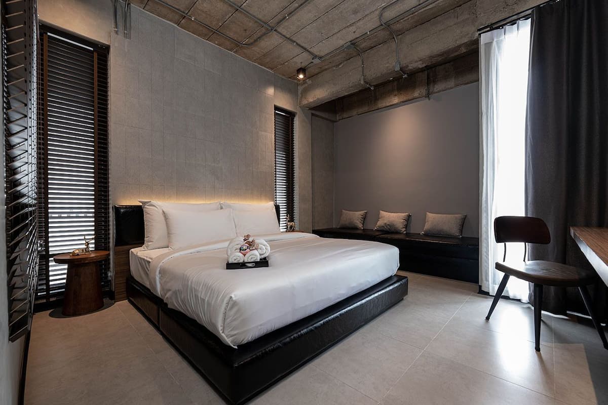 Um quarto moderno com uma cama grande, uma mesinha de cabeceira, uma cadeira e uma janela com persianas.