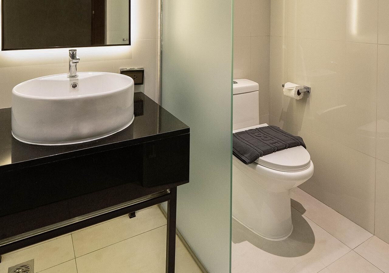 A modern bathroom with a white sink, black countertop, and a toilet with a towel on the seat.