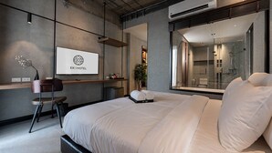 A modern hotel room with a large bed, a desk, and a shower area visible through a glass door. - EXII Hotel Ngamwongwan (Nonthaburi)