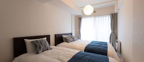 Una habitación de hotel con dos camas, una lámpara en el techo, una ventana con cortinas y un equipo de aire acondicionado.