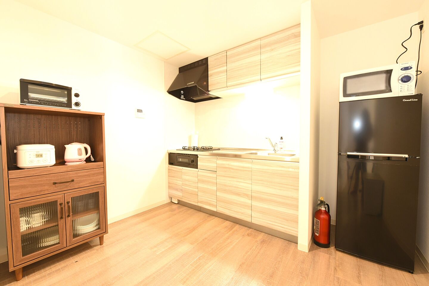 A compact kitchen with wooden cabinets, a built-in microwave, a gas stove, and a black refrigerator.