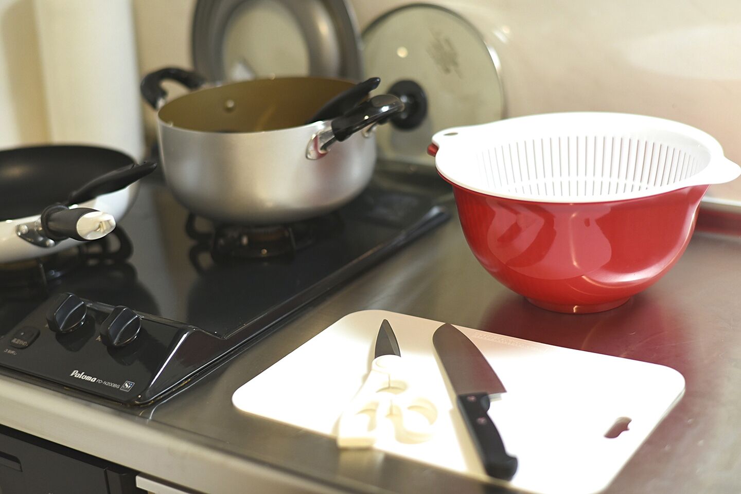 Une cuisinière avec une casserole, une passoire rouge et un couteau sur une planche à découper.