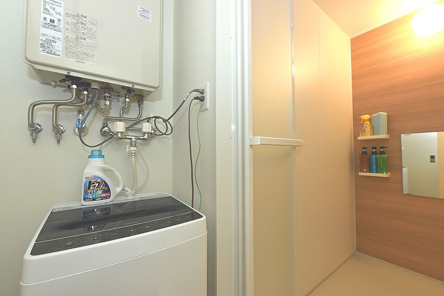 Un baño con lavadora incorporada, un lavamanos con una botella de detergente y una pared de madera con un espejo y repisas.