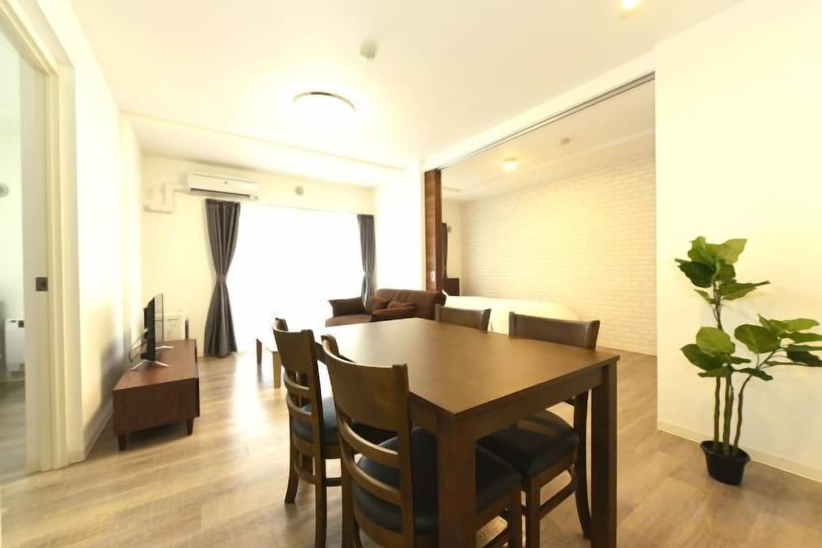 Uma sala de jantar com mesa e cadeiras de madeira, uma mesinha lateral e um vaso com planta.