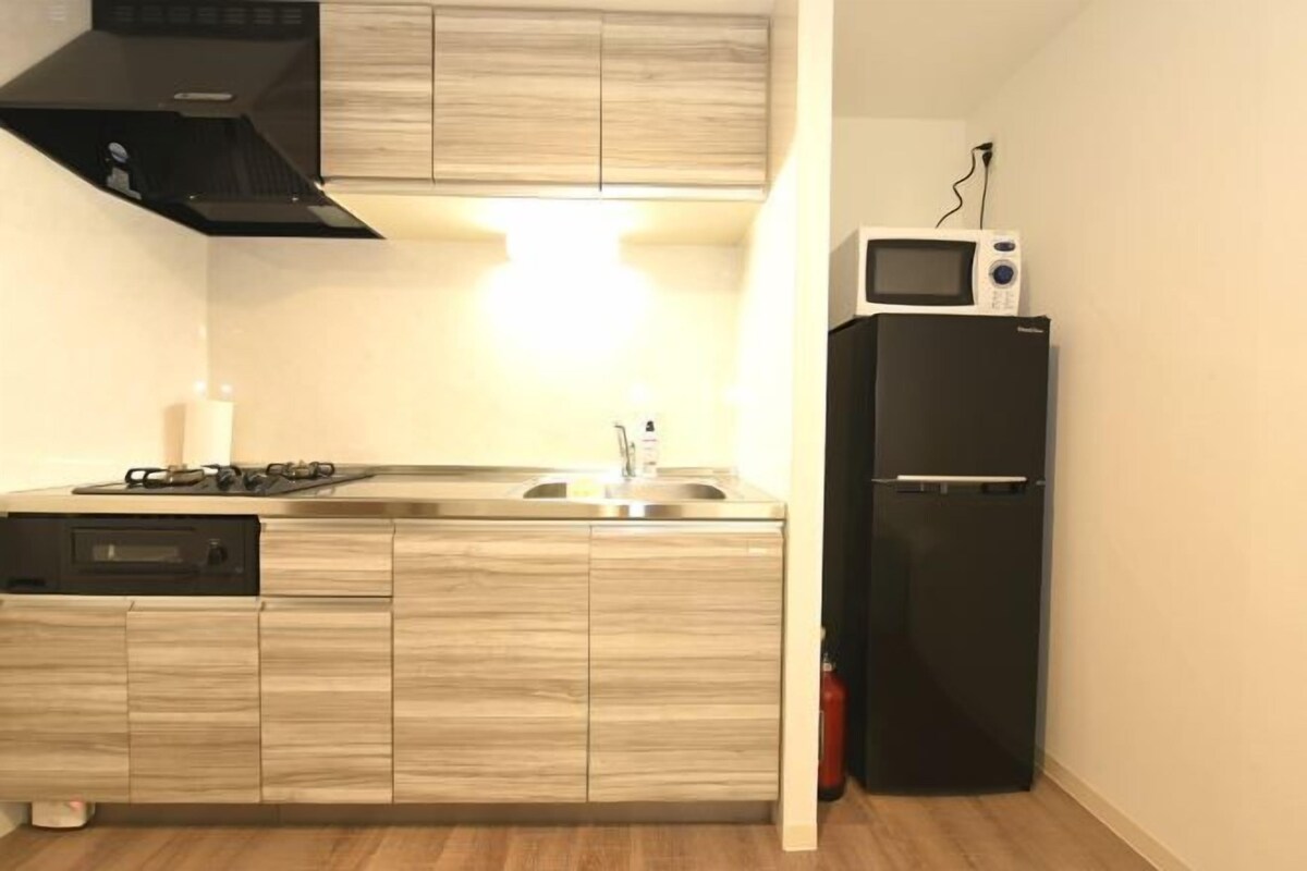 Een compacte keuken met een ingebouwde magnetron, een zwarte koelkast en een fornuis.