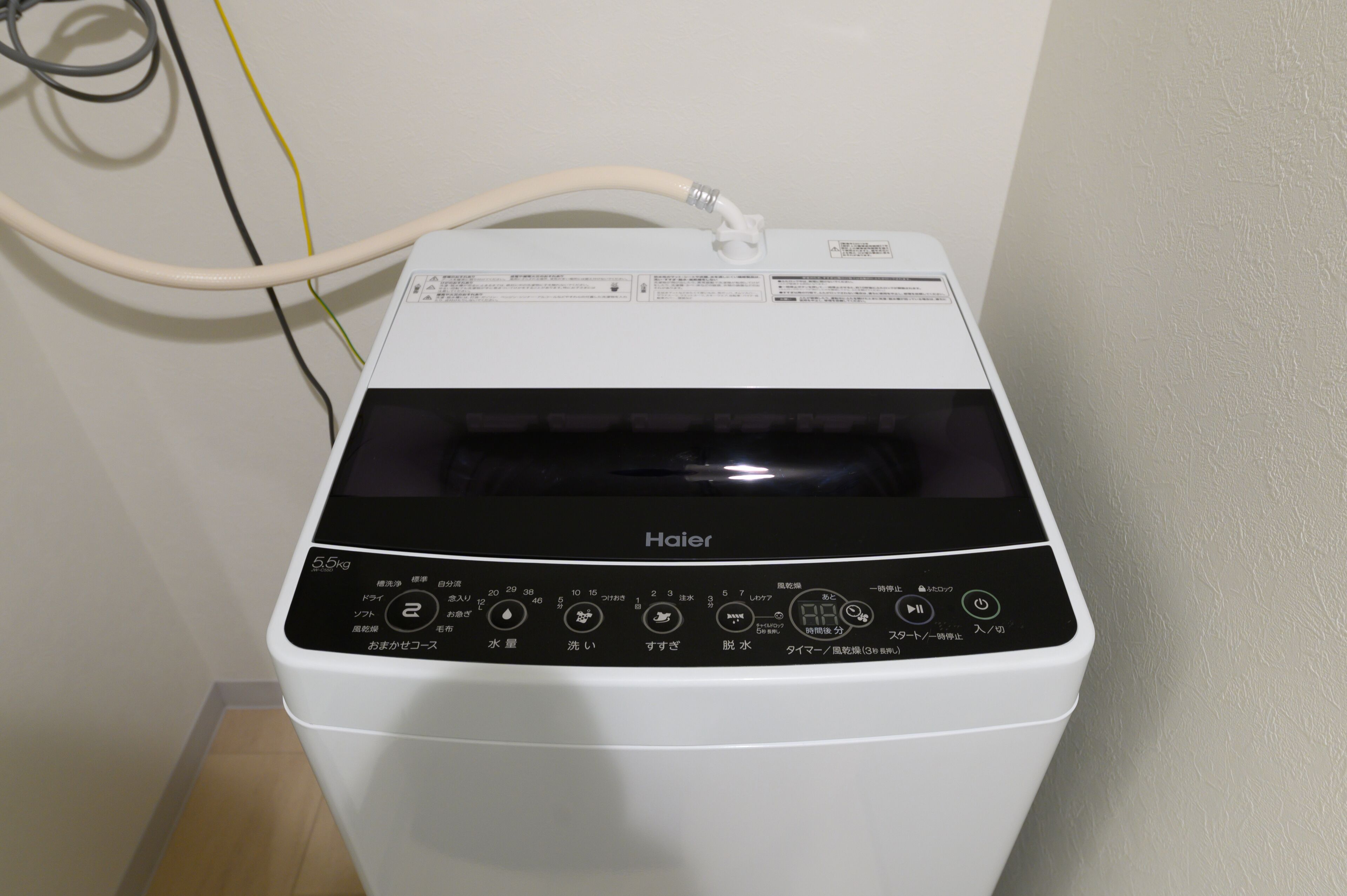 A white Haier washing machine with a control panel and a hose.
