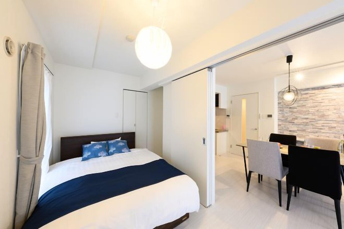 Een moderne hotelkamer met een groot bed, een zithoek met een tafel en stoelen, en een keuken die door een open deur zichtbaar is.