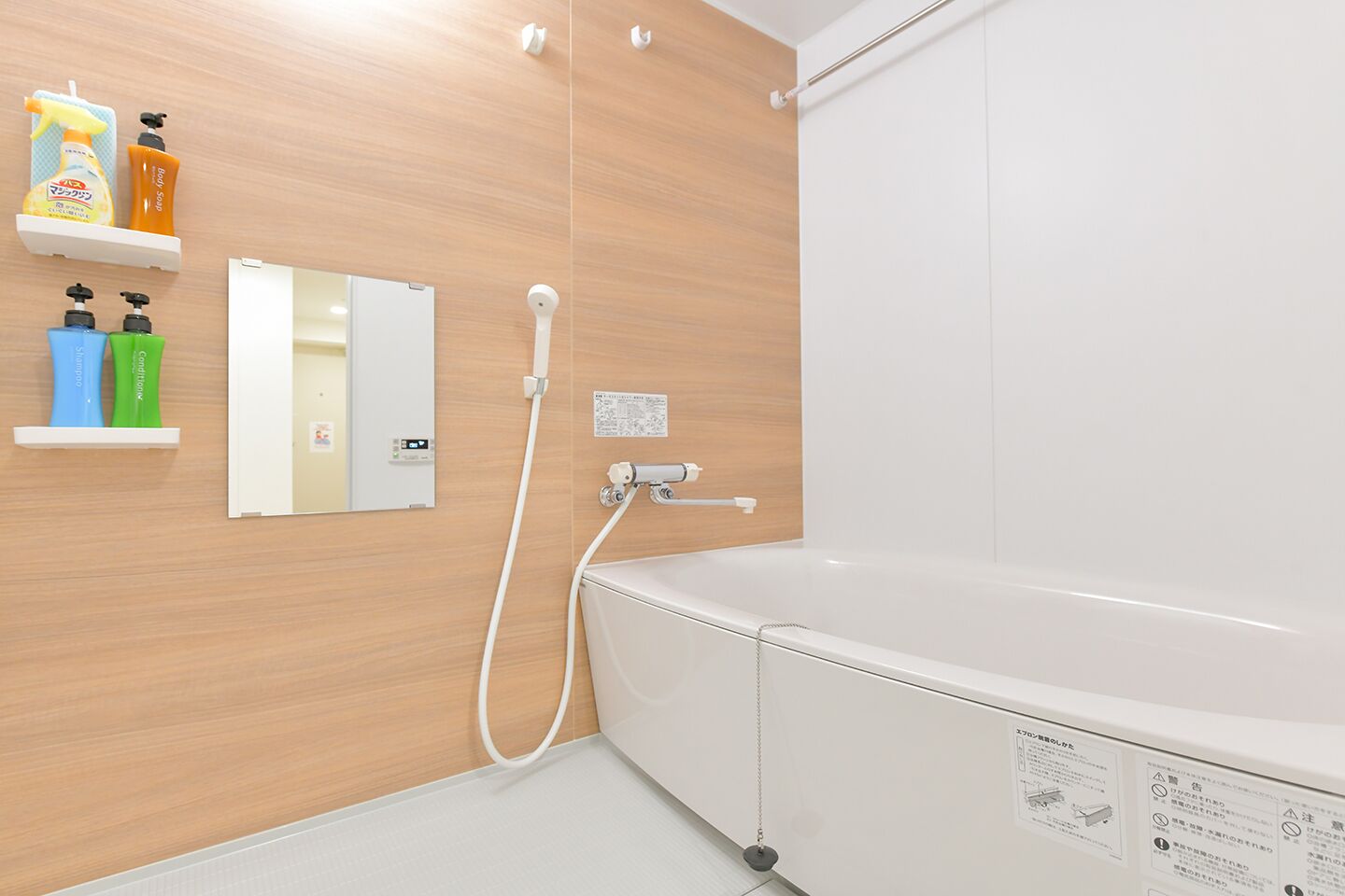 Un bagno moderno con una parete in legno, una vasca da bagno bianca e uno specchio. Sono presenti mensole con articoli da toilette e un pannello di controllo per la doccia.
