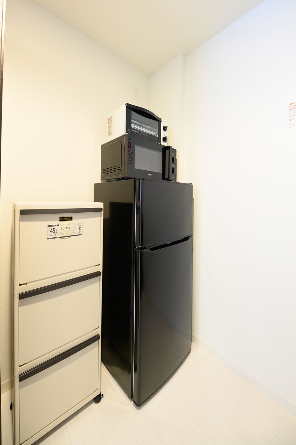 Un refrigerador negro con un microondas encima, un gabinete blanco con cajones, y un piso de color claro.