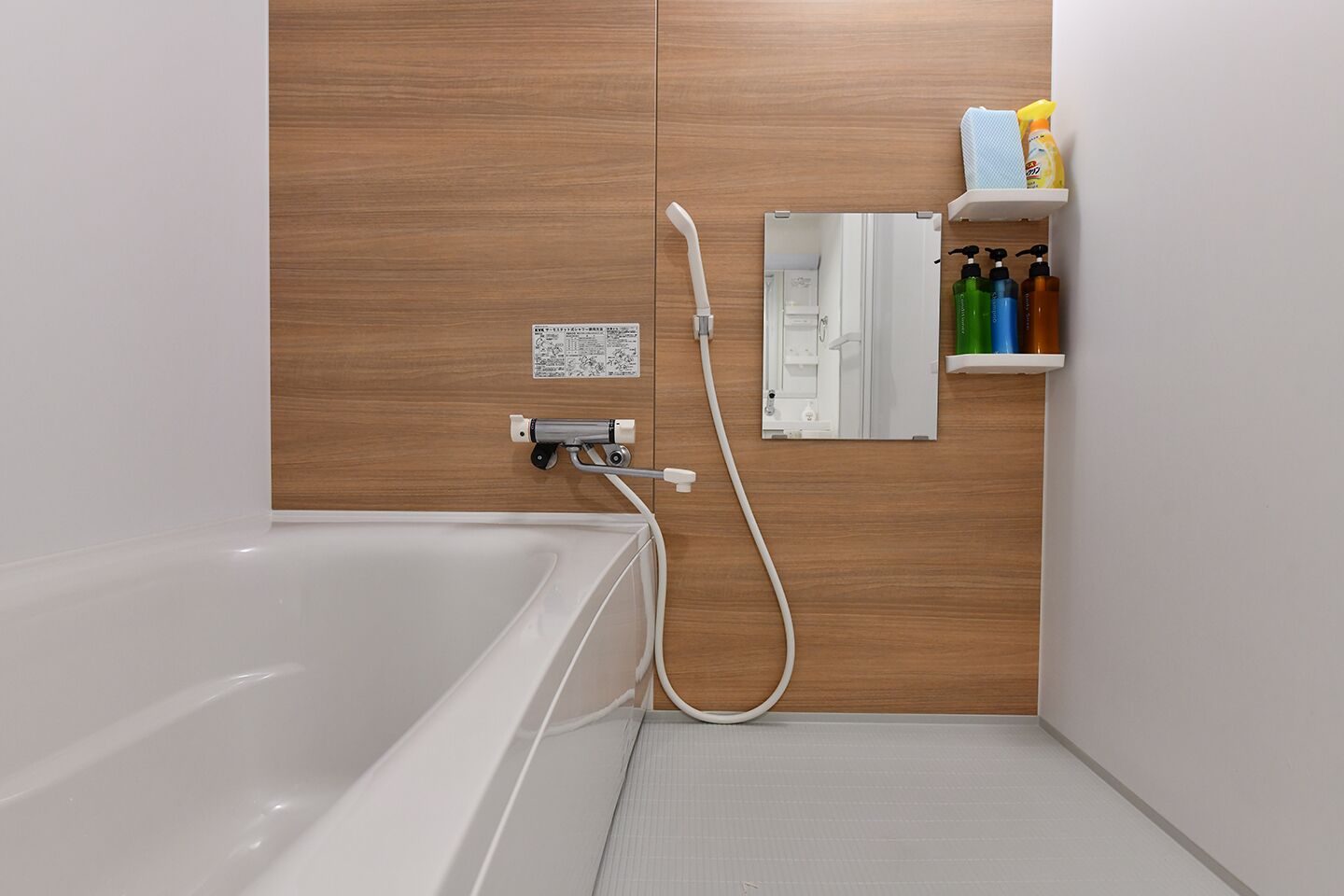 A modern bathroom with a white bathtub, wooden paneling, a built-in shower, and a shelf with toiletries.