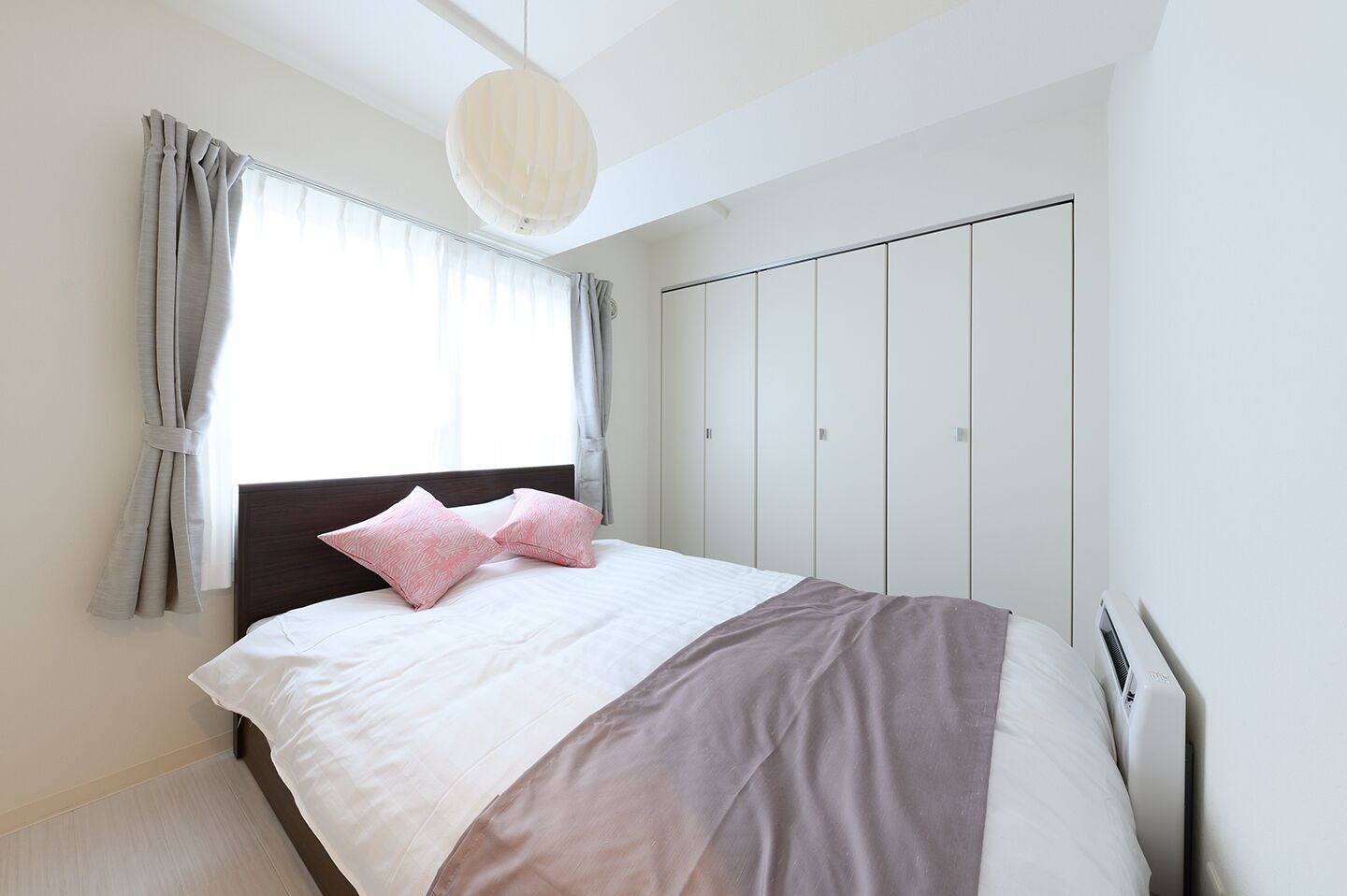 A bedroom with a bed, curtains, a wardrobe, and a hanging light fixture.