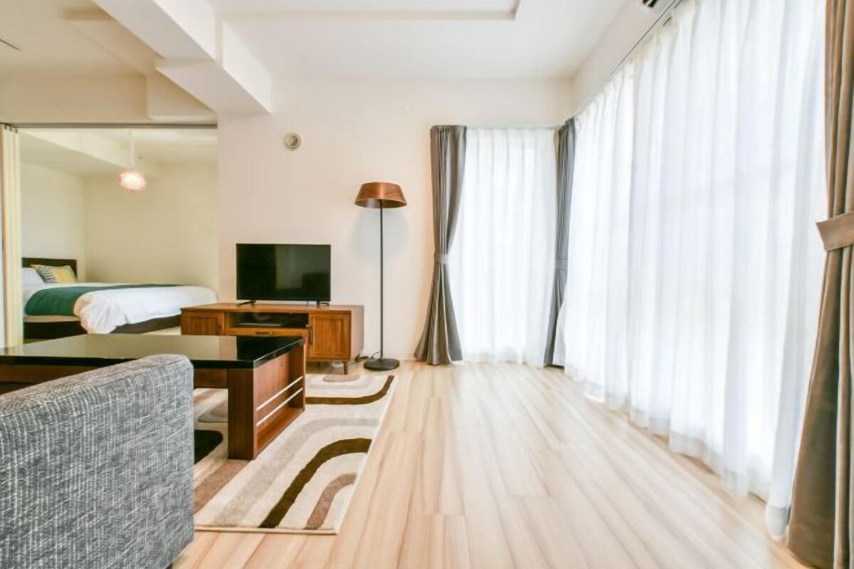 Een hotelkamer met een bed, een televisie, een bank, een lamp en een groot raam met gordijnen.