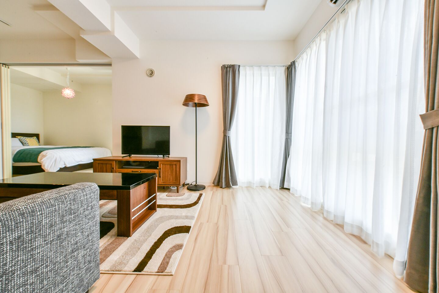 A modern hotel room with a bed, a TV, a desk, and a large window with curtains.