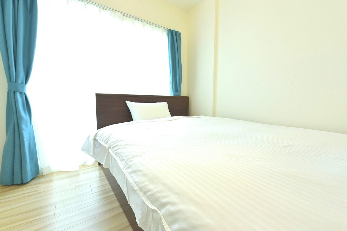 A hotel room with a bed, a wooden floor, and blue curtains.