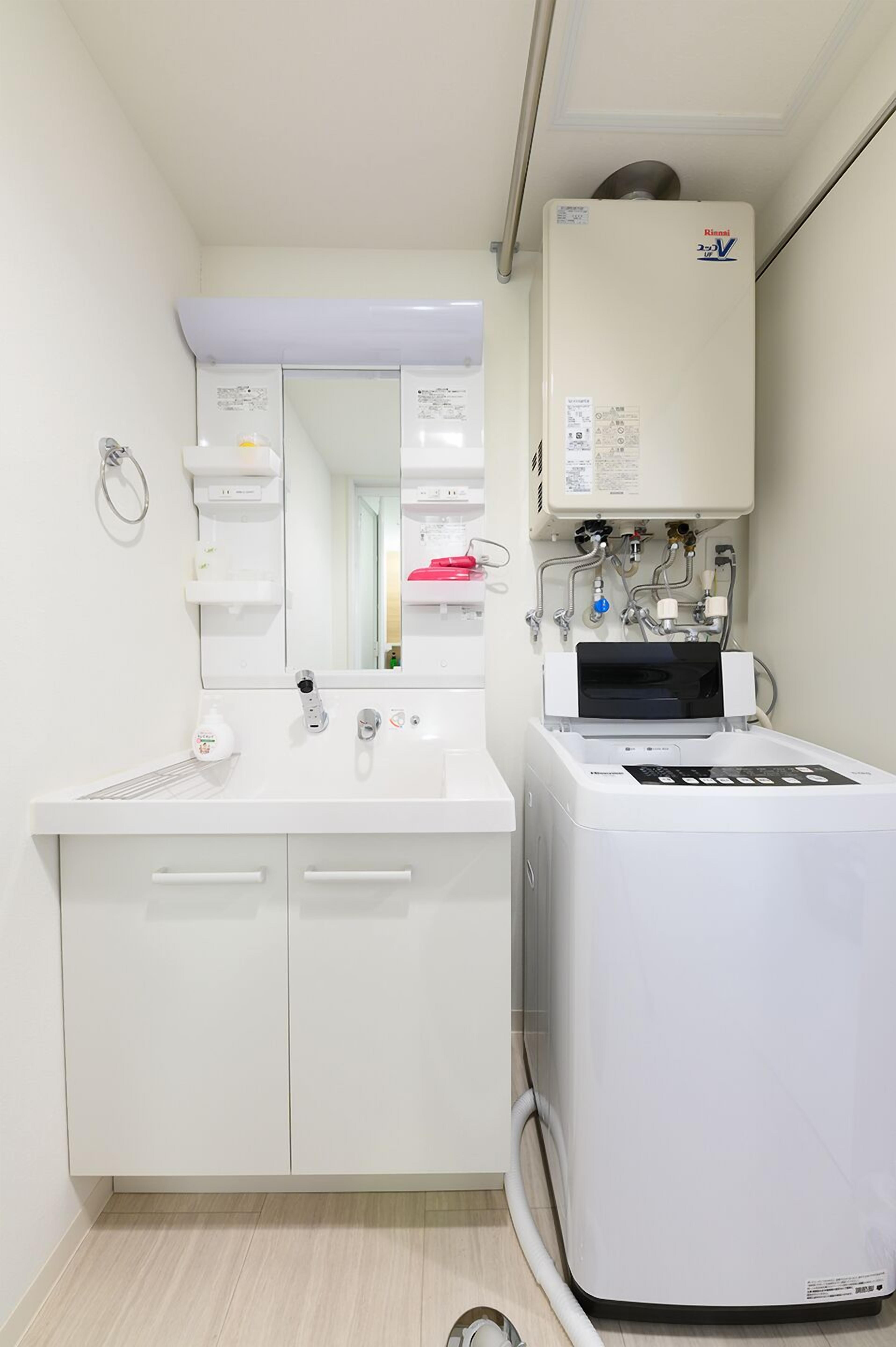 A bathroom with a white sink, mirror, and a white washing machine.