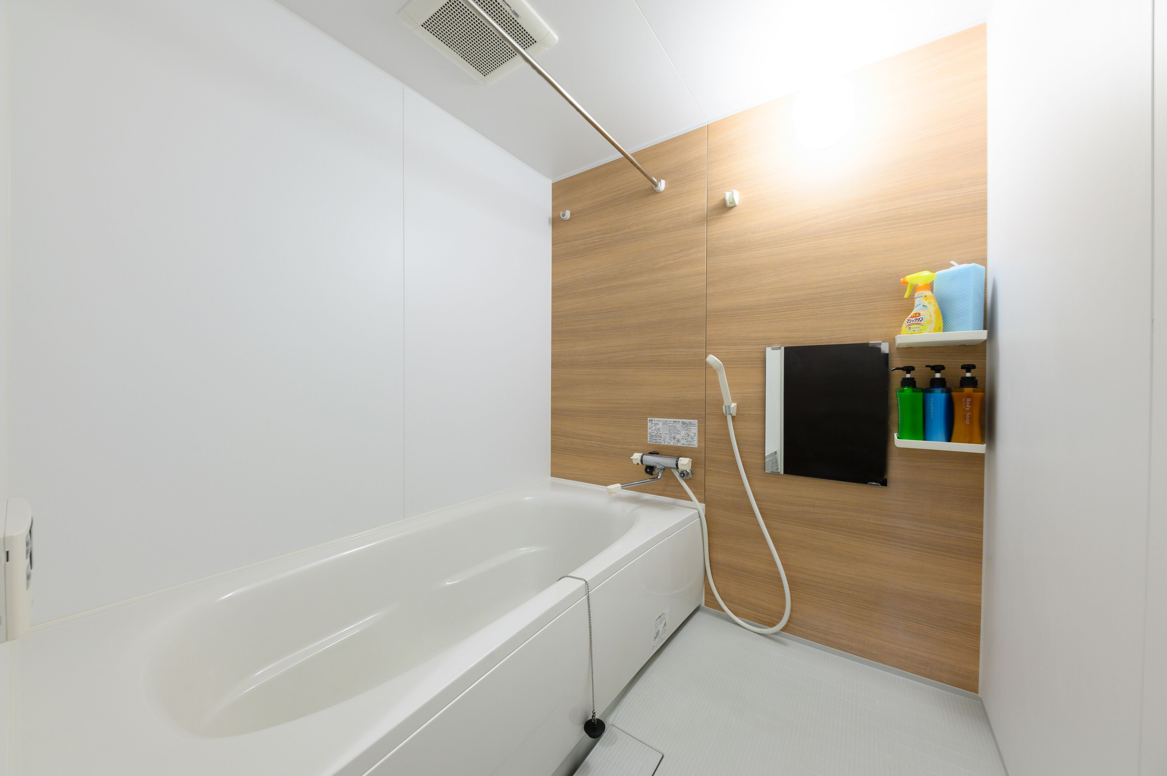 A modern bathroom with a white bathtub, wooden panel wall, and a shelf with toiletries.