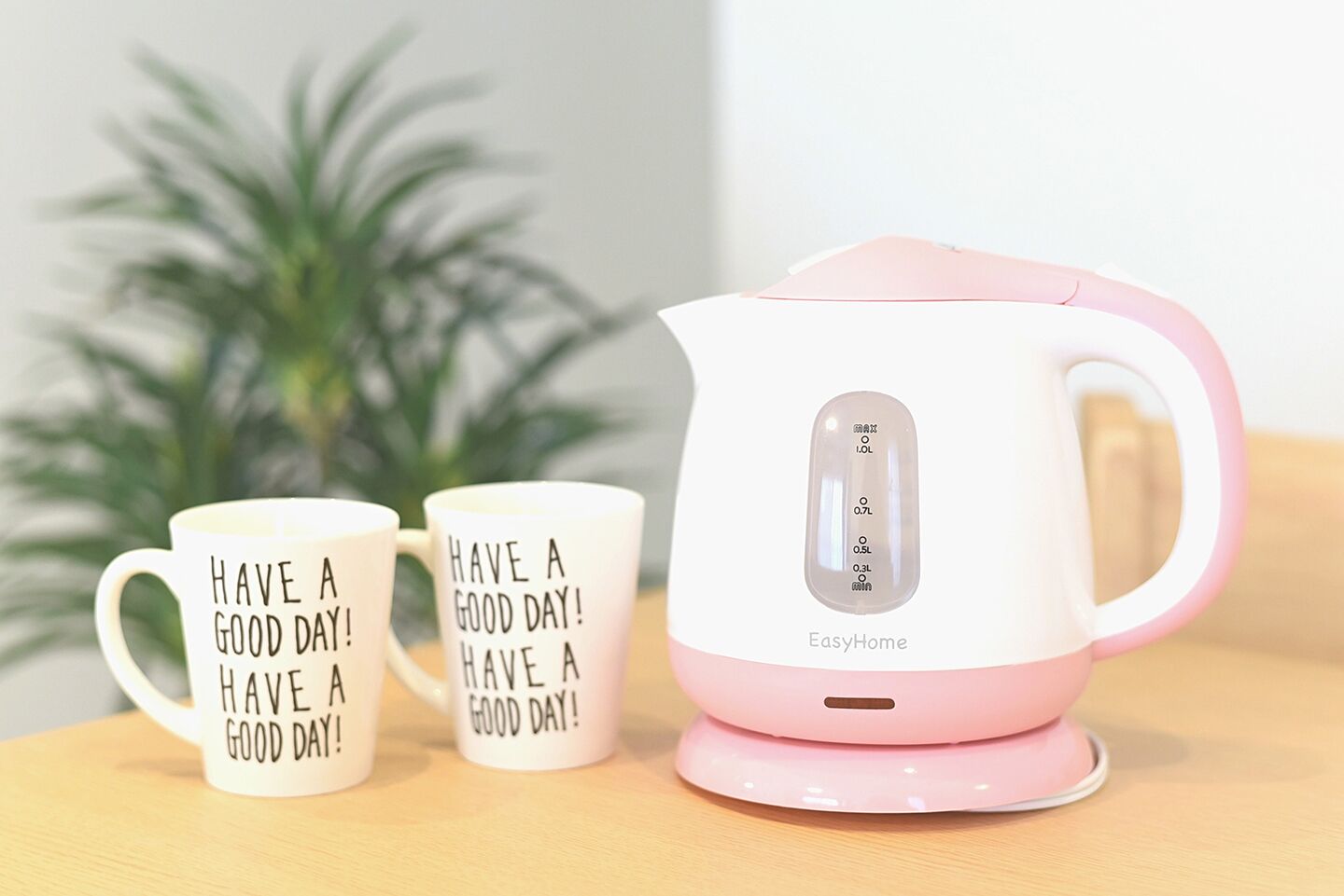 Dos tazas blancas con el texto negro "HAVE A GOOD DAY!" y una tetera eléctrica rosa y blanca con marcas de nivel.