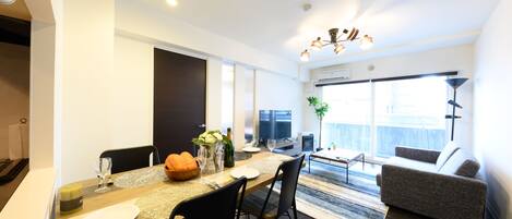 A modern living room with a sofa, a dining area with a table set for two, and a large window providing a view of the outdoors.