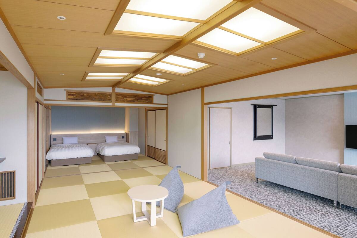 A modern hotel room with a checkered floor, two beds, a sofa, a small table, and a TV mounted on the wall.