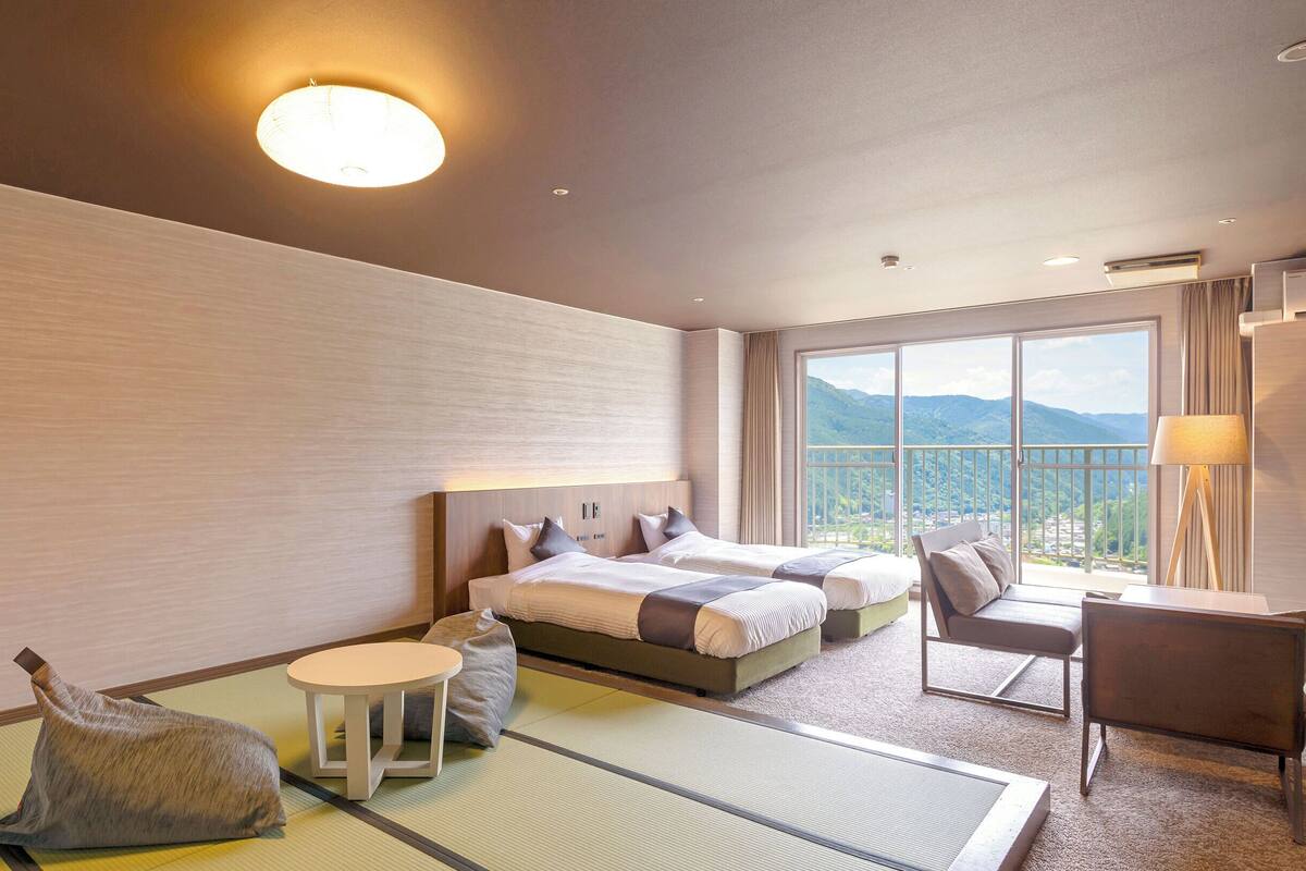A hotel room with a large bed, a sofa, a small table, and a view of mountains through the window.