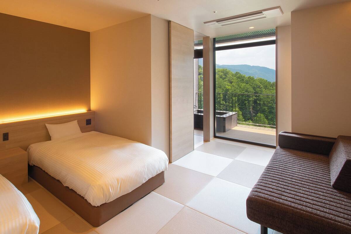 A modern hotel room with two beds, a sofa, and a balcony with a view of the mountains.