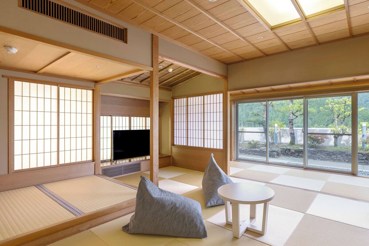 A traditional Japanese room with tatami flooring, a television, and a view of a garden.