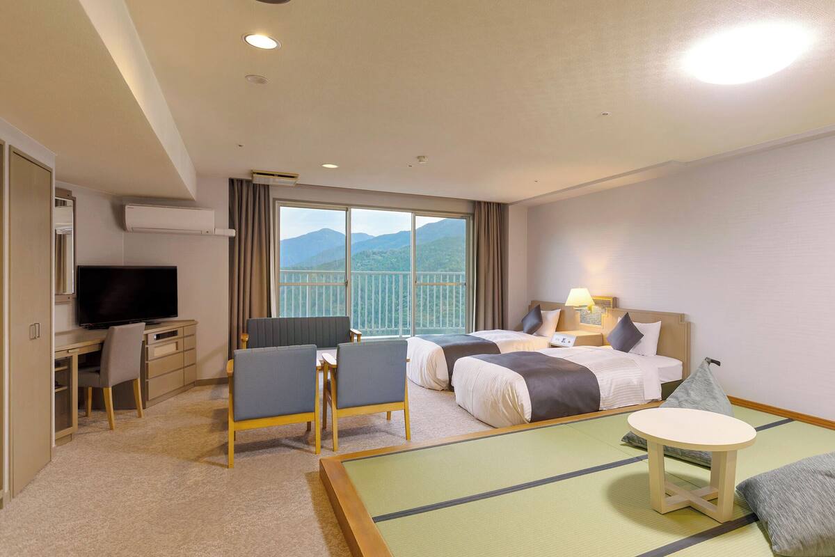 A hotel room with two beds, a desk, a television, and a view of mountains.
