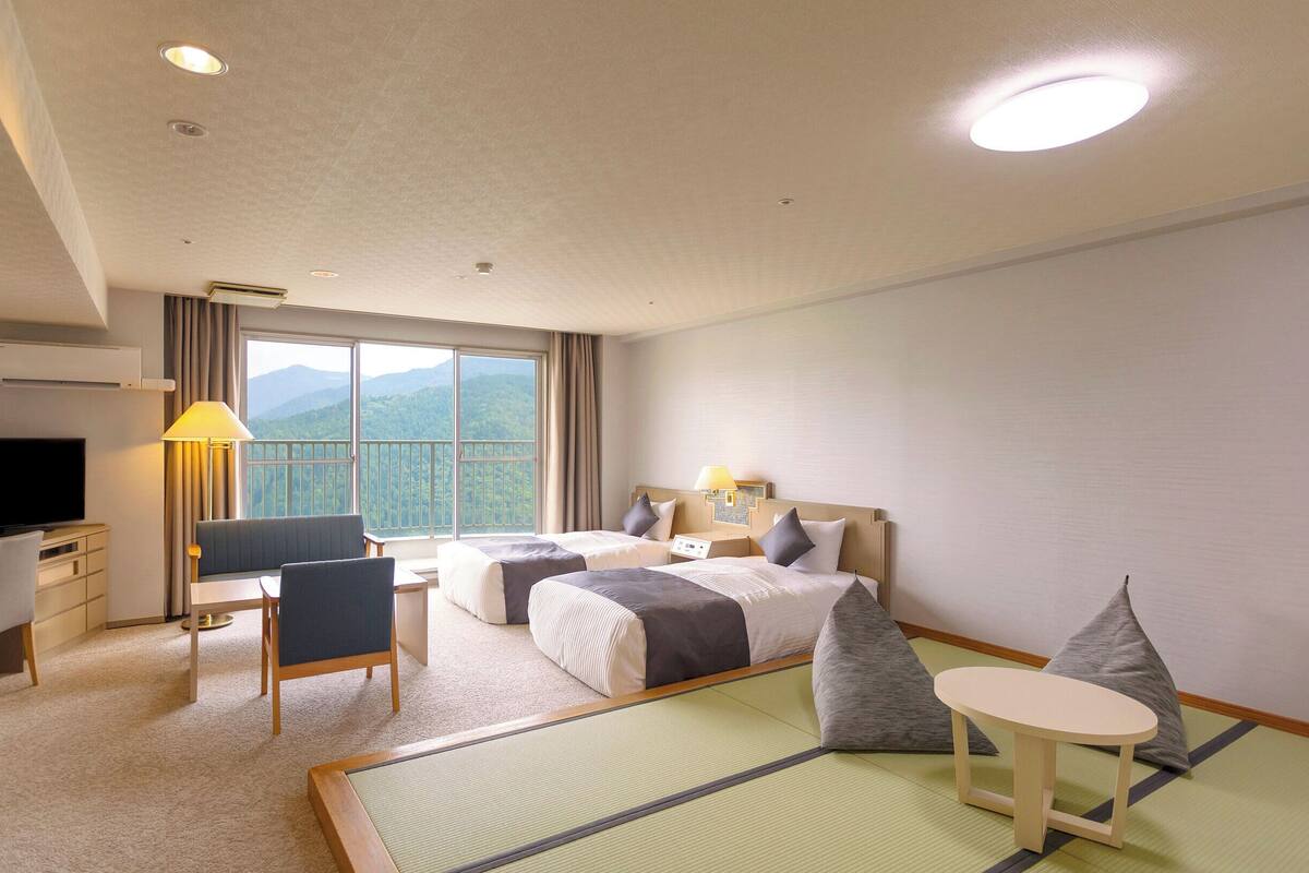 A hotel room with a large bed, a desk with a chair, a television, and a view of mountains through the window.