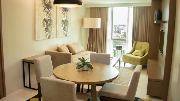 A modern living room with a round dining table, beige sofas, a green armchair, and a large abstract painting on the wall. - The Padgett Suites Cebu (Cebu City)