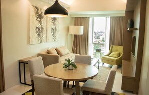 A modern living room with a round dining table, beige sofas, a green armchair, and a large abstract painting on the wall.