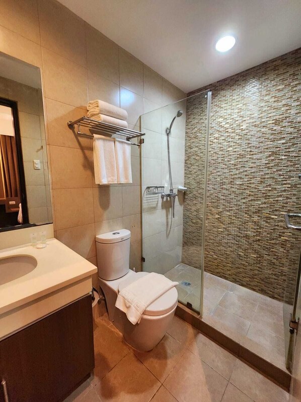 A modern bathroom with a glass-enclosed shower, a toilet, and a sink with a mirror.