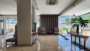 A spacious lobby with a high ceiling, a central seating area with chairs and a small table, and a large window offering a view of the outdoors. - The Padgett Suites Cebu (Cebu City)